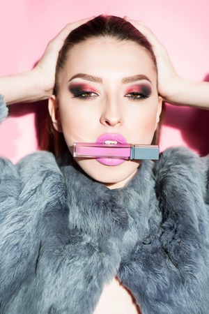 Pretty sexy cute woman or girl with long brunette hair and fashion makeup in gray fur with pink lipstick on studio wall backgroundの写真素材