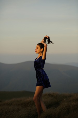 Pretty sexy cute young woman or girl with long windy hair in dark blue dress on natural background in sunsetの写真素材