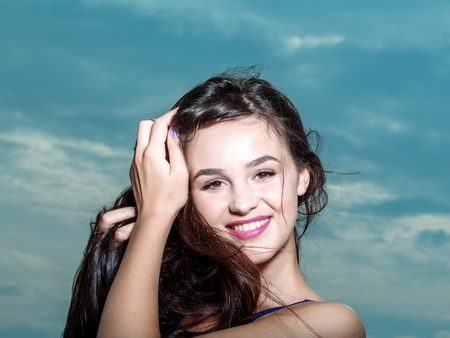 Young pretty woman or girl with cute sexy happy smiling face and long brunette hair in blue vest posing outdoor on cloudy sky backgroundの写真素材