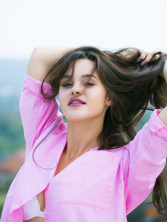 Young pretty woman or girl with cute sexy face and long brunette hair in pink shirt posing outdoor on blurred backgroundの写真素材