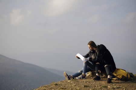 Two pretty girls young women friends travelers with map explore route outdoors on mountain top on...