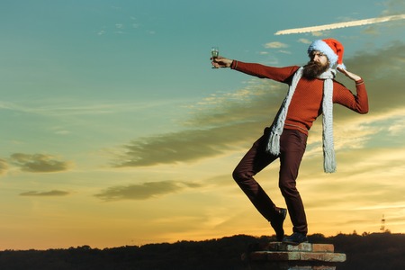 young bearded santa claus man with long beard in red sweater pants and new year hat in scarf at...