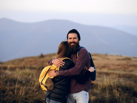 Romantic couple of woman or girl and handsome bearded man embrace on cliff over mountain tops outdoor with yellow backpackの写真素材