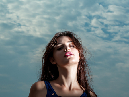 Young pretty woman or girl with cute sexy face and long brunette hair in blue vest posing outdoor on cloudy sky backgroundの写真素材
