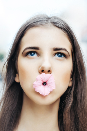 Young woman beautiful brunette girl model with long hair and blue eyes holds pink flower in mouth outdoorsの写真素材