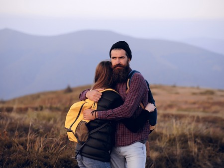 Romantic couple of woman or girl and handsome bearded man embrace on cliff over mountain tops outdoor with yellow backpackの写真素材