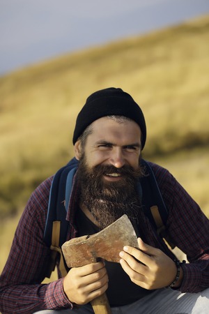 lumberjack handsome bearded man hipster with long beard and moustache in gray shirt with axe in hand smiling on mountain top on foggy skyの写真素材