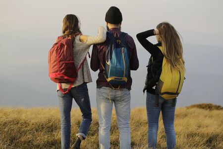 Bearded handsome man with two pretty sexy cute girls or women standing with colorful backpacks a on mountain topの写真素材