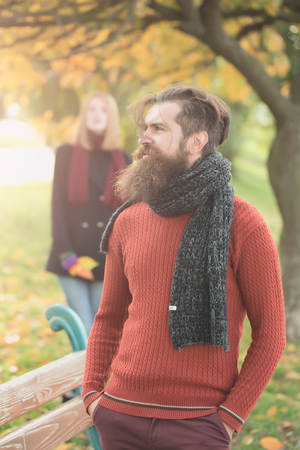 Bearded man hipster with beard and moustache dating with pretty girl near bench outdoors in autumn park on natural backgroundの写真素材