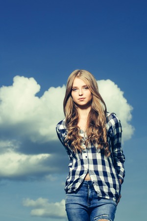 Pretty girl young beautiful woman with long curly blond hair in shirt poses outdoors on blue skyの写真素材