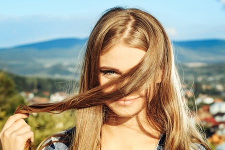 Pretty girl cute young woman with long curly beautiful blond hair flirts outdoors against sky on natural backgroundの写真素材