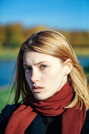Pretty girl young beautiful woman with red hair and scarf outdoors in park on autumn day on natural backgroundの写真素材