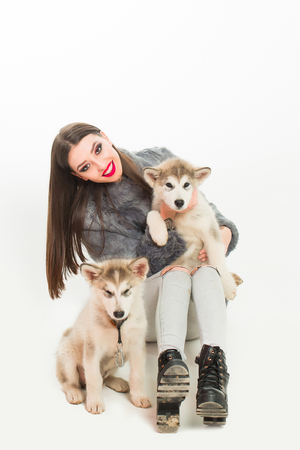 pretty sexy brunette woman or girl with long hair and fashion makeup in fur coat with cute little dogs or puppy of husky pet isolated on white backgroundの写真素材