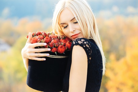 Pretty cute girl or beautiful blond woman in sexy black dress with red rose flowers in box outdoor...