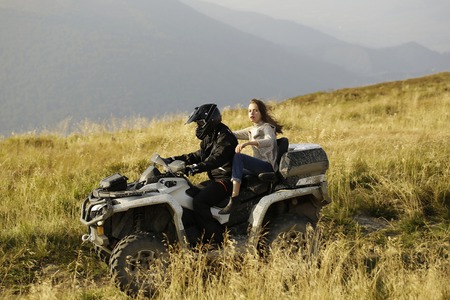 Handsome man and pretty girl ride quad bike on field road on mountain scene