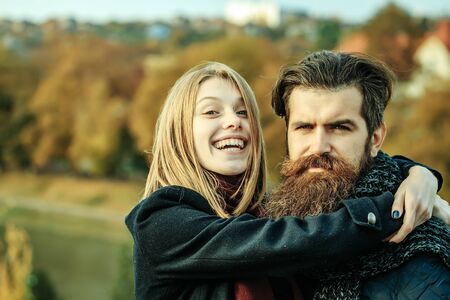 Young happy couple of pretty girl and bearded man hipster embracing outdoors in park on autumn day on natural backgroundの写真素材