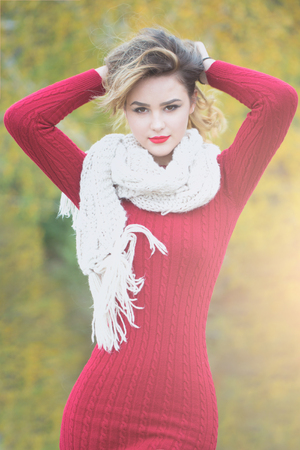 young pretty sexy woman or girl with cute face and long blond hair has red lipstick on lips in dress and scarf outdoor on green natural backgroundの写真素材
