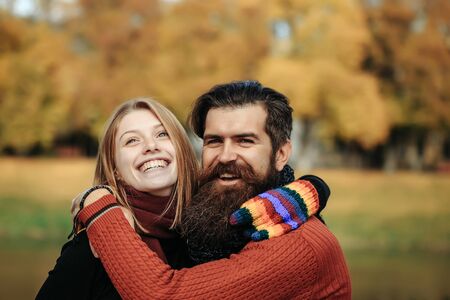 Young happy couple of pretty girl and bearded man hipster embracing outdoors in park on autumn day...