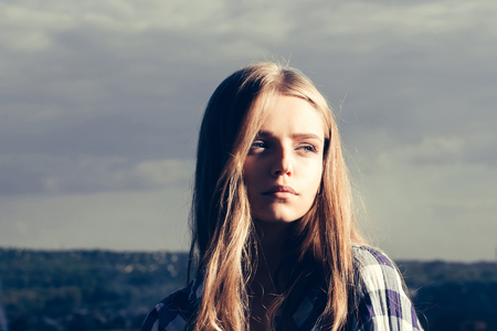 Pretty girl young beautiful woman with blue eyes and long blond hair in shirt poses outdoors on natural backgroundの写真素材