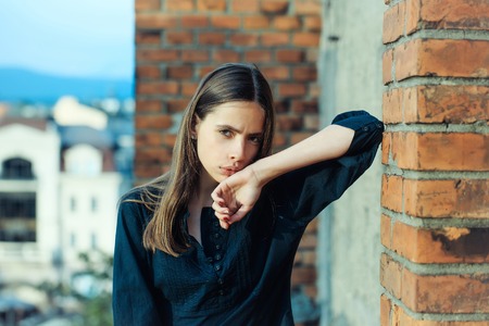 Pretty girl young beautiful woman with long brunette hair outdoors on roof at brick wallの写真素材