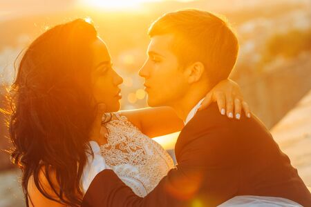 Young newlyweds couple of pretty bride woman and groom with handsome face hugging and looking at each other in sunny wedding day on streetscape background outdoorの写真素材