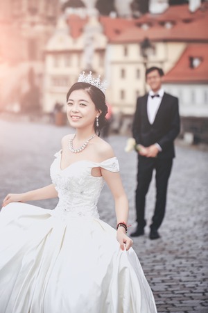 Chinese cute happy smiling bride and groom young newlyweds just married couple in streets of old city on wedding day with flowersの写真素材