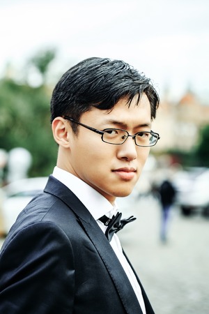 Chinese groom handsome man in elegant suit stands in wedding costume with bow tie on old cityscapeの写真素材