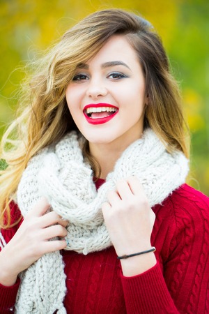 young pretty sexy woman or girl with cute smiling face and long blond hair has red lipstick on lips in dress and scarf outdoor on green natural backgroundの写真素材