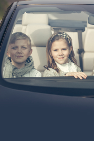 Couple of cute baby children friends of girl and boy people at wheel pretends driving car as drivers on road outdoorの写真素材