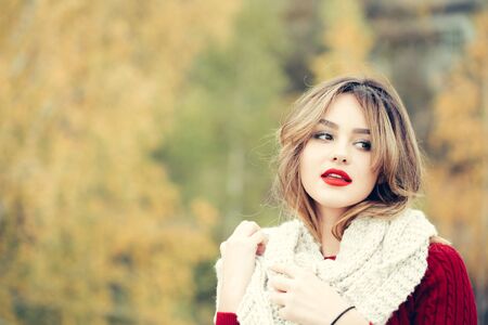 young pretty sexy woman or girl with cute face and long blond hair has red lipstick on lips in dress and scarf outdoor on green natural background, copy spaceの写真素材