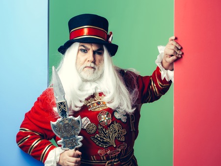 Frown senior man beefeater yeomen warder or male royal guard bodyguard in red uniform with spear on green wallの写真素材