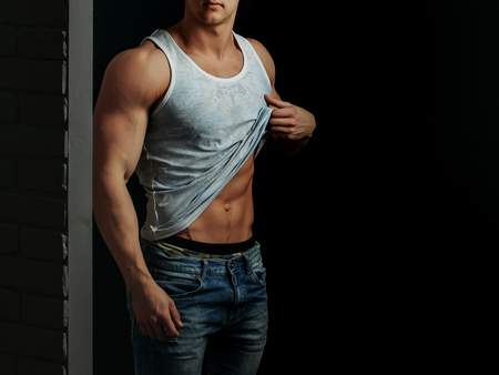 young handsome macho man with sexy muscular athletic body with bare torso and strong belly with six packs or abs in white vest on black background, copy spaceの写真素材