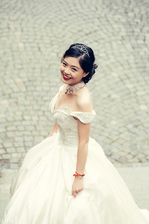Chinese cute happy smiling bride just married beautiful young asian cute sexy woman with brown eyes and red lips in crown outdoorsの写真素材