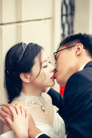 Chinese cute bride and groom young newlyweds just married couple kiss on streets of old city on wedding dayの写真素材