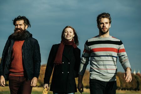 Young people friends of pretty cute sexy girl or woman and two bearded men outdoors in park on autumn sunny day on natural blue sky backgroundの写真素材