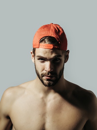 Handsome man sexy young bearded male model with beard in red cap topless with nude torso and sexi body on grey backgroundの写真素材