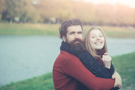 Young happy couple of pretty girl and bearded man hipster embrace outdoors in park on autumn day on natural background near water, copy spaceの写真素材