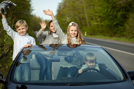 Cute four baby children friends of girls and boys people with at wheel pretends driving car as drivers on road outdoorの写真素材