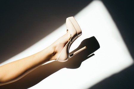Female leg beautiful sexy slim foot in fashionable elegant beige high heel shoe lying indoors on sunny grey floorの写真素材