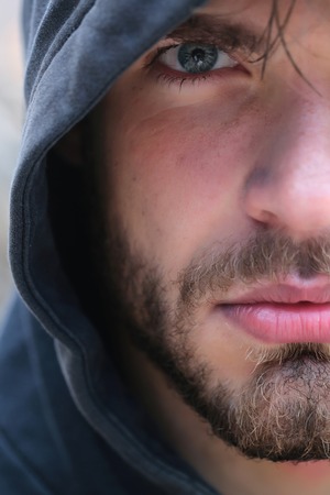 Bearded man young handsome guy male with beard and half face grey eye in hood on head outdoorsの写真素材