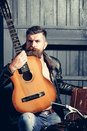 Frown bearded man with beard moustache and gray hair stylish hipster male with guitar outdoors on wooden backgroundの写真素材