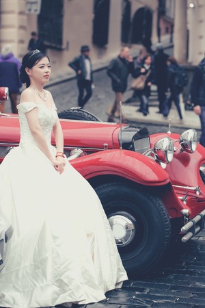 Pretty girl bride young chinese cute sexy woman in long white wedding dress stands outdoors near red retro carの写真素材