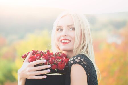 Pretty cute girl or beautiful blond woman in sexy black dress with red rose flowers in box outdoor...