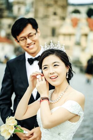 Chinese cute happy smiling bride and groom young newlyweds just married couple in streets of old city on wedding day with flowersの写真素材