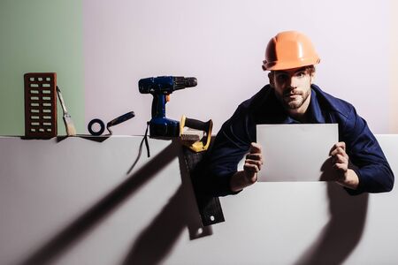 Serious man handsome bearded male builder repairman craftsman foreman or construction worker in orange hard hat with tools keeps blank paper for copy space in hands on white backgroundの写真素材
