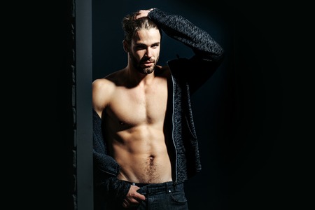 young handsome bearded sexy macho man with long beard and stylish hair in jacket and pants with muscular bare torso in studio on black and brick wall background, copy spaceの写真素材