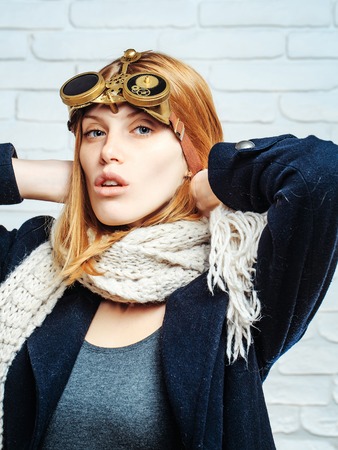 Pretty girl young cute beautiful woman or watchmaker with watch mechanical metallic gears and cogwheels on red hair on white brick wallの写真素材