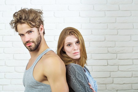 Young couple of handsome man or muscular macho in grey undershirt with pretty cute girl or beautiful woman in knitted coat on white brick backgroundの写真素材