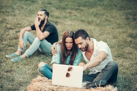 Young people or friends relax handsome man smokes while love couple of pretty girl girlfriend and boyfriend watch laptop computer on natural backgroundの写真素材