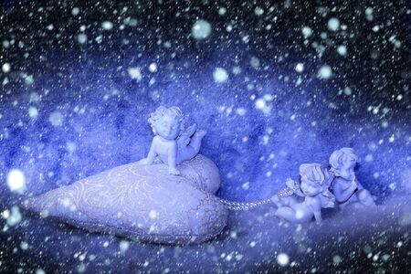 beautiful new year figurine composition of cupid angels for valentine day or christmas with small pillow in shape of heart on white wadding decorating snow with bright light sparks under snowflakesの写真素材